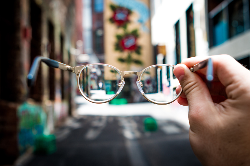 Looking down a city while holding glasses out to refocus