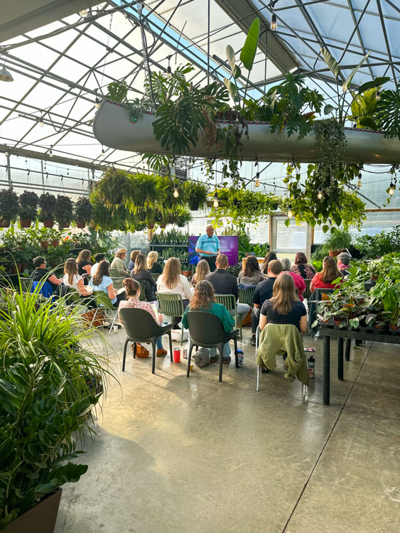 Crowd of people seated in a greenhouse with a presenter addressing them